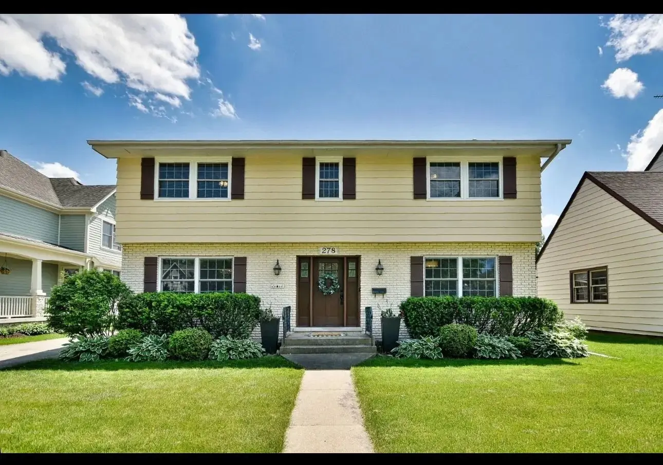 <p>Create a highly realistic picture that showcases a stylish and inviting exterior renovation of a two-story suburban house covering around 2,000 square feet. This house features a crisp white paint job which contrasts with the fashionable black window frames, completed with a sophisticated wooden front door. Add some sleek modern light fixtures and a porch that boasts sleek design adorned with wooden decking. Include a well-maintained, minimalistic garden teeming with carefully trimmed hedges and an array of vibrant flowers. Illustrate an open and sunny front lawn boasting carefully positioned landscape lighting.</p>
