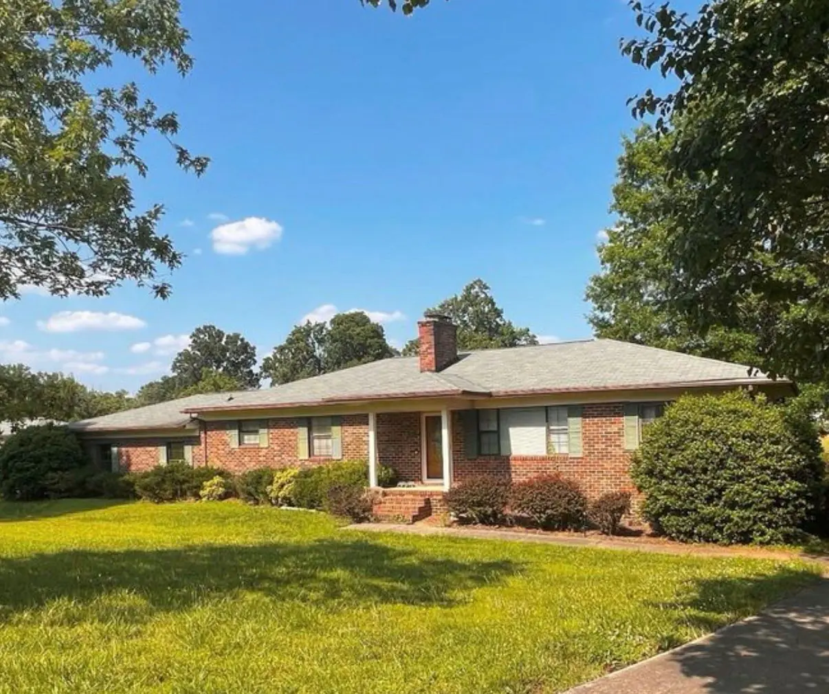 <p>Create a highly realistic image of an exterior view of a renovated single-story brick ranch-style house, showcasing modern curb appeal. The house has black shutters replacing the previous green ones. Its windows have been refashioned with black frames, and the front door boasts a modern design, constructed with wood and complemented by glass panels. The front porch spans the entire front facade, acting as a welcoming space under the shelter of a simple roof extension. A stone walkway stretches up to the upgraded porch. The overgrown bushes are replaced by manicured landscaping, characterized by vibrant flowers and neatly trimmed shrubs. The lawn is lush, with healthy, well-maintained grass. The house is styled with a modern aesthetic, featuring clean lines and a harmonious color palette. It embodies an aura of natural light and a sense of openness. The house measures approximately 60 feet in width and 30 feet in depth, offering a compelling visual with an aspect ratio of 16:9 and a version 5 style. The image skill level is set to 'expressive', highlighting the fine detailing and the striking elements of the ranch-style house.</p>
