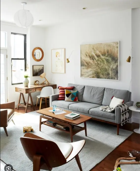 <p>Create an image showcasing a highly detailed and photorealistic interior design of a modern living room, measuring about 15ft x 18ft. Maintain a neutral color scheme complemented by occasional pops of color. Feature a large, plush sectional sofa in a warm beige tone, situated against the far wall. Introduce a round glass coffee table with a brass frame in place of the former coffee table. Transform the desk area into a sleek bar area furnished with a dark wood bar cabinet, and adorned with a mirrored backsplash and brass accents. Above the bar, display floating shelves filled with glassware and bottles. Update the artwork with a large, abstract piece primarily displaying gold and neutral hues. Substitute the rug with a plush, geometric patterned rug in cream and gray tones. Improve the lighting with a contemporary chandelier hanging over the seating area and recessed lighting scattered around the room. Let the ambiance exude sophistication, comfort, and functionality, highlighting clean lines and high-end materials. Allow natural light to pour in through a wide window. Keep the aspect ratio of the image as 3:2 with a level of verbosity of 5.</p>