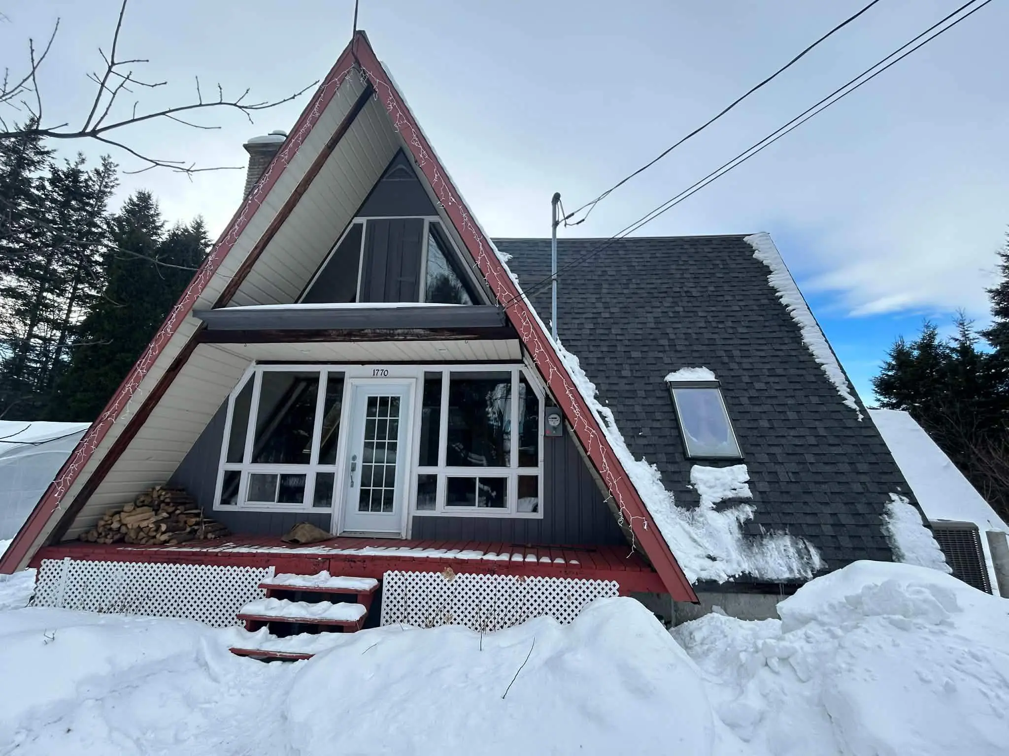 <p>Generate a photorealistic, high-resolution image of an A-frame cabin during winter. The cabin is renovated, painted in a warm gray tone with white trims, and features a sleek, modern entrance. The porch is 10ft deep and 20ft wide, made of gray composite decking with a minimalist black railing. The solid wood front door is adorned with frosted glass panels. A stylish outdoor seating area can be seen next to the door, featuring two contemporary Adirondack chairs and a circular fire pit. The roof is made of dark gray metal, and a large, energy-efficient window replaces the triangular one above the door, providing panoramic views. The surrounding landscape is snow-clad with evergreen trees in the background. The image should encapsulate a modern, cozy, and inviting winter retreat.</p>